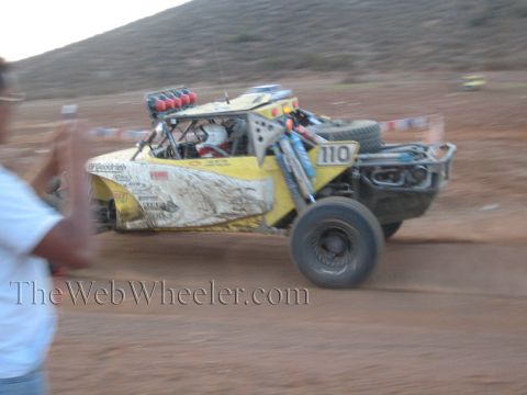 1990 Ford Bronco - Yellow off-road race truck number 110 with BFGoodrich livery races across a desert course as a spectator watches.