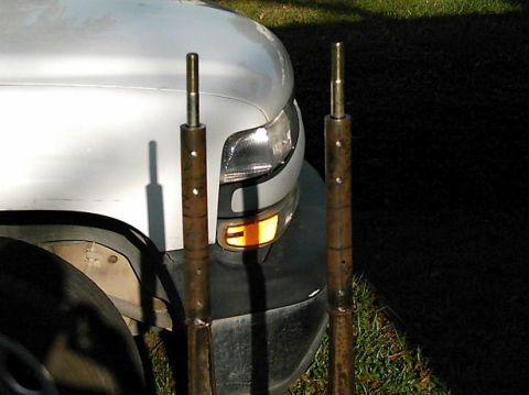 1986 Ford Bronco - Two metal rods are positioned in front of the headlight and wheel well of a white truck.
