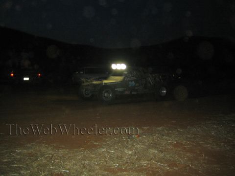 1990 Ford Bronco - yellow off-road race buggy with an illuminated roof light bar runs at night across a dark desert course.