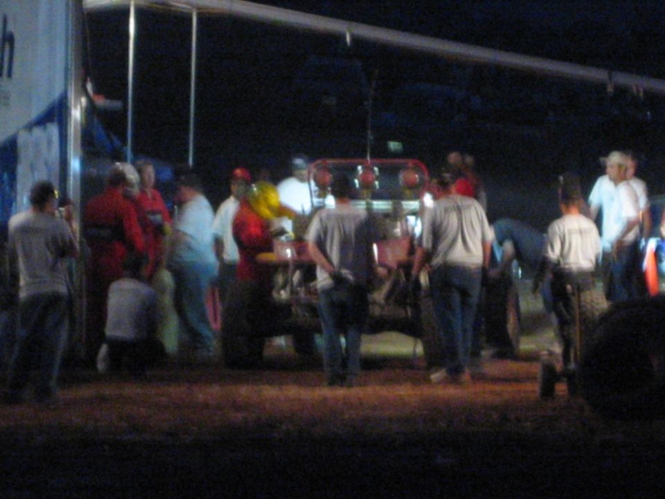 Crowd around an off-road race car beside a hauler trailer at night