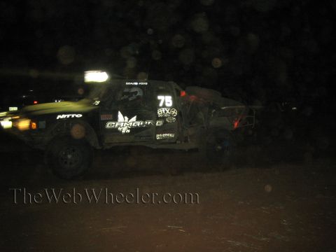 1990 Ford Bronco - number 75 off-road desert race truck speeds through the dark with its roof light bar illuminated and Nitto sponsor decals visible.