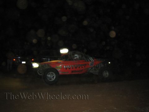 1990 Ford Bronco - orange Hutchins-branded number 1003 off-road race buggy speeds through the dark with its roof light bar lit.