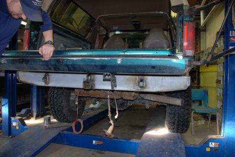 1996 Ford Bronco - A mechanic works on the custom rear bumper of a green Ford Bronco, which appears to be from the early to mid-1990s.