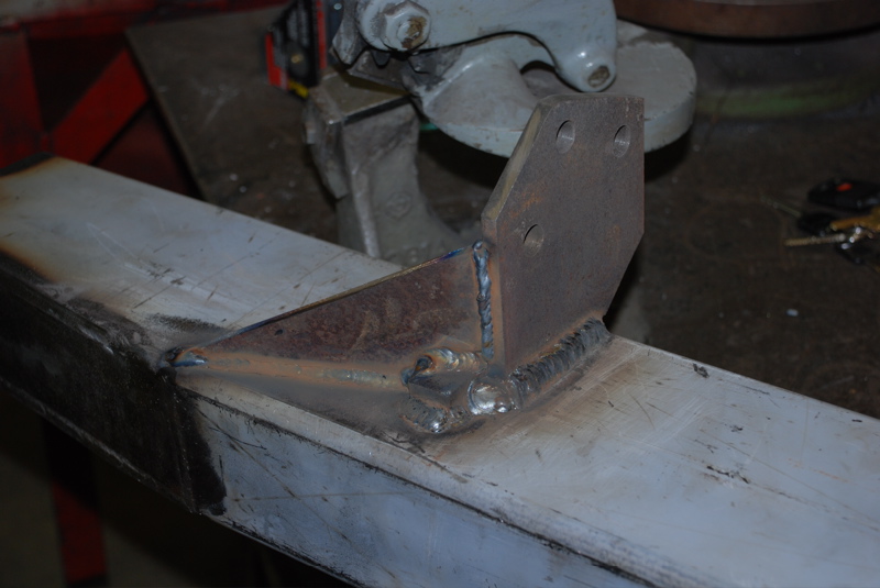 Close-up of a metal bracket welded onto a frame section. It has two bolt holes