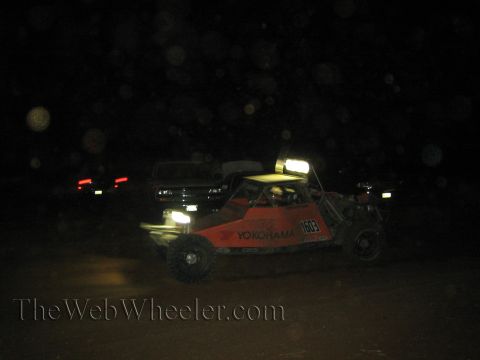 1990 Ford Bronco - orange off-road race buggy with Yokohama decals and number 1603 runs at night, taillights of other vehicles glowing behind.