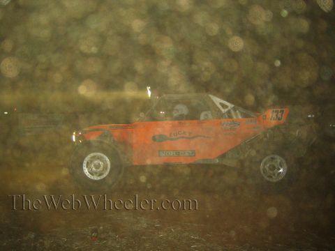 1990 Ford Bronco - orange number 133 off-road race buggy with Norcat and Lucky decals races at night through a dusty, hazy frame.