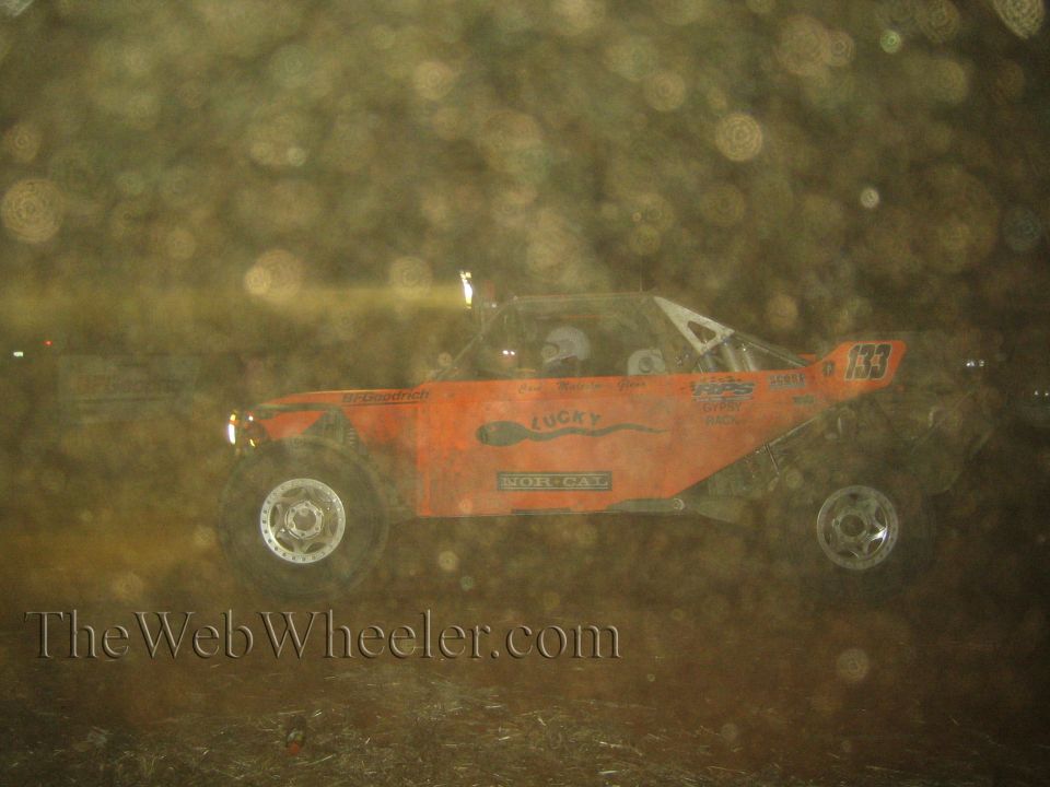 Orange Norcat number 133 off-road buggy at night through dusty haze