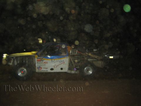 1990 Ford Bronco - white and blue off-road race truck with Mango Racing decals races at night on a dark dirt course.