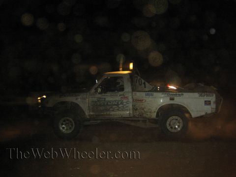 1990 Ford Bronco - white number 701 off-road race truck with Victory and BFGoodrich decals races at night kicking up dust.