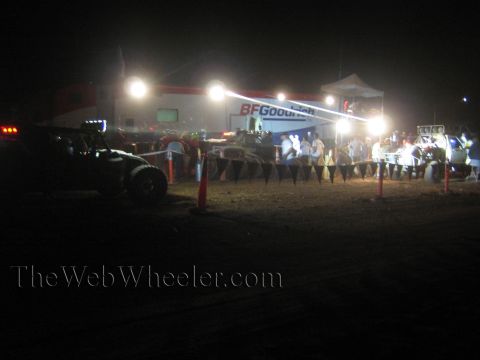 1990 Ford Bronco - off-road race pit area at night with a BFGoodrich tent, floodlights, traffic cones and a crowd watching a race vehicle.