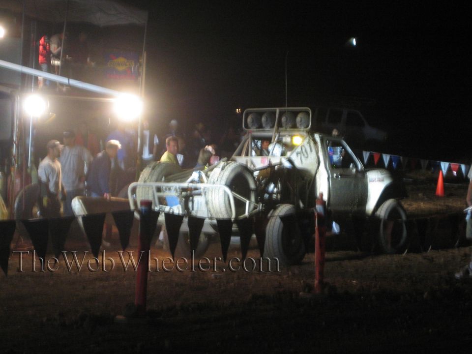 White off-road race truck in pit at night with crew and spectators