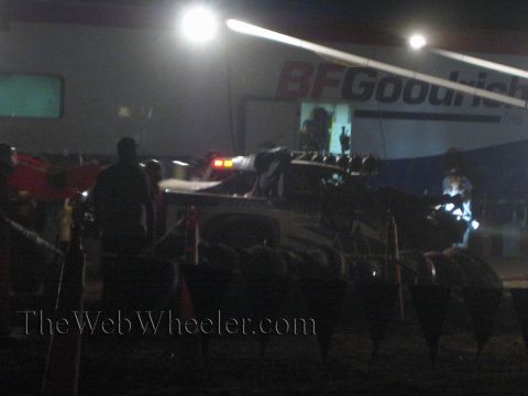 1990 Ford Bronco - off-road race truck sits in a floodlit pit at night under a large BFGoodrich banner with crew silhouettes around it.