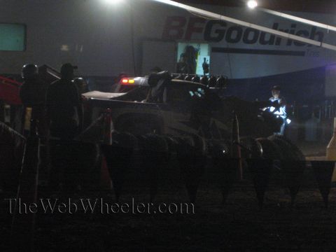 1990 Ford Bronco - Crew members stand around an off-road race truck in a floodlit pit at night beneath a BFGoodrich banner.