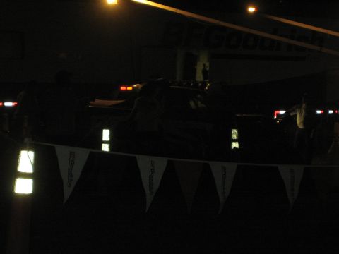 1990 Ford Bronco - very dark nighttime race pit scene showing BFGoodrich pennant bunting, faint vehicle lights and silhouetted people.