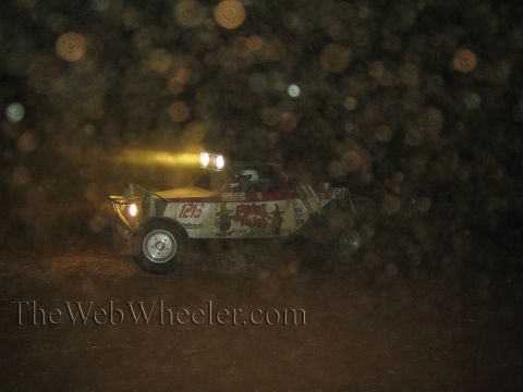 1990 Ford Bronco - open-cockpit off-road race buggy marked 1213 races through the dark with headlights and roof lights blazing, kicking up dust.