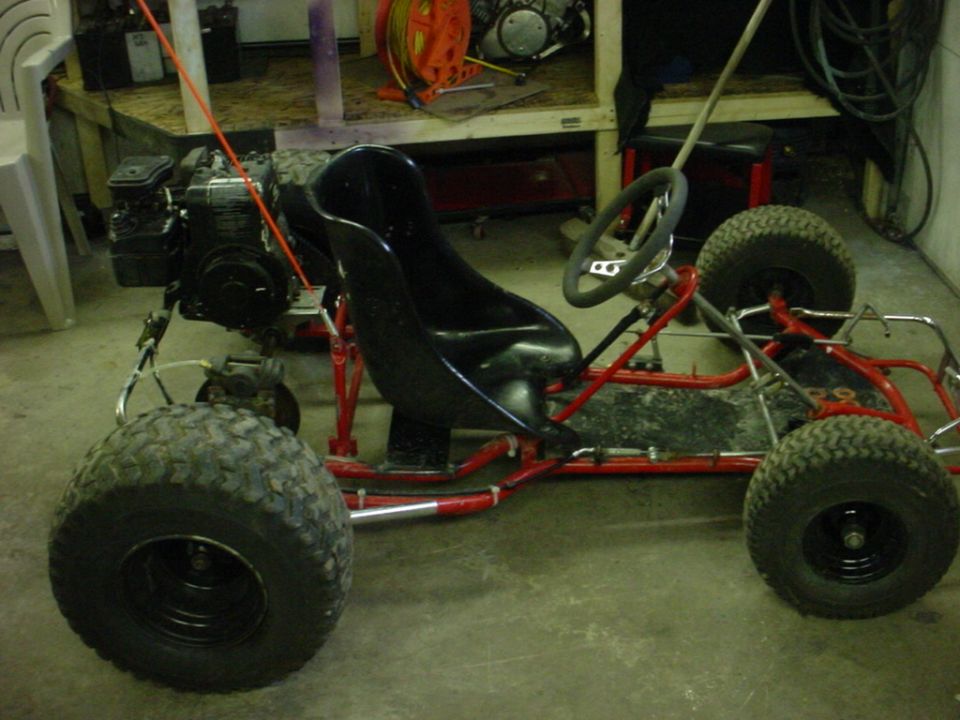 Go-kart with red frame, black seat, and large tires. Engine is visible