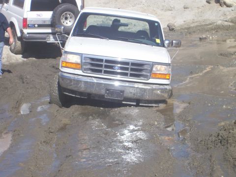 1993 Ford Bronco - A white 1993 Ford Bronco navigates a muddy trail, with another Bronco visible behind it.