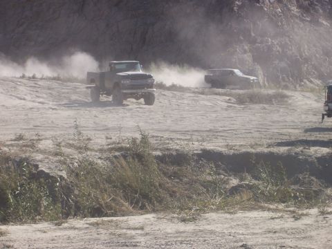 1993 Ford Bronco - Off-road trucks navigate a dusty track, kicking up clouds of dirt.