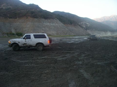 1993 Ford Bronco - Two vehicles navigate a muddy terrain with hills in the background.