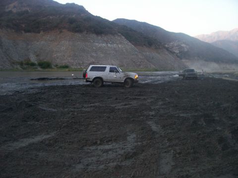1993 Ford Bronco - A white 1992 Ford Bronco navigates a muddy terrain, with another vehicle visible in the distance.