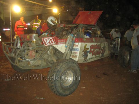 1990 Ford Bronco - Crew members in safety gear surround the number 1213 off-road buggy, its rear deck raised, during a nighttime pit stop on red dirt.