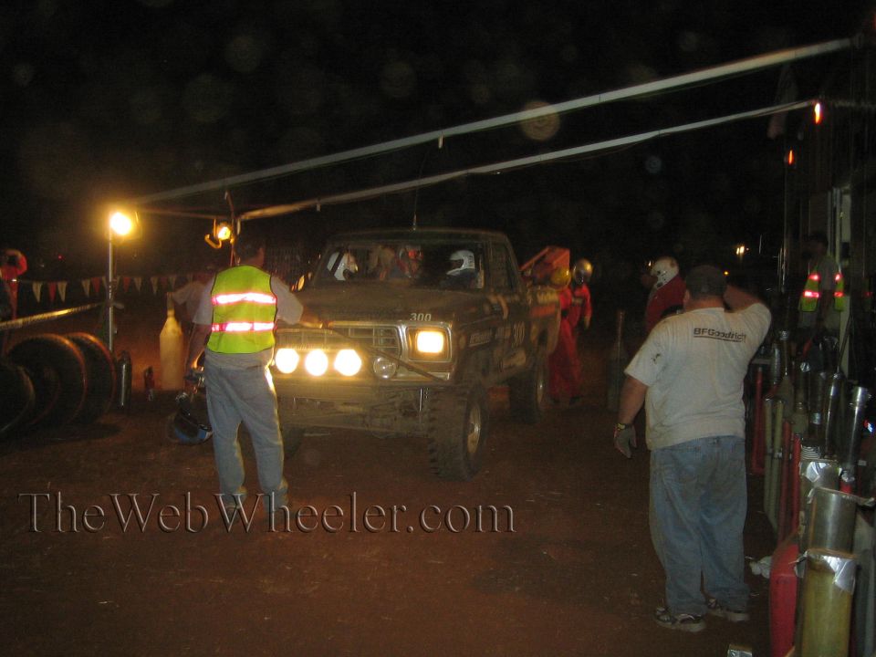 Dark number 300 off-road truck at night pit with crew and lights