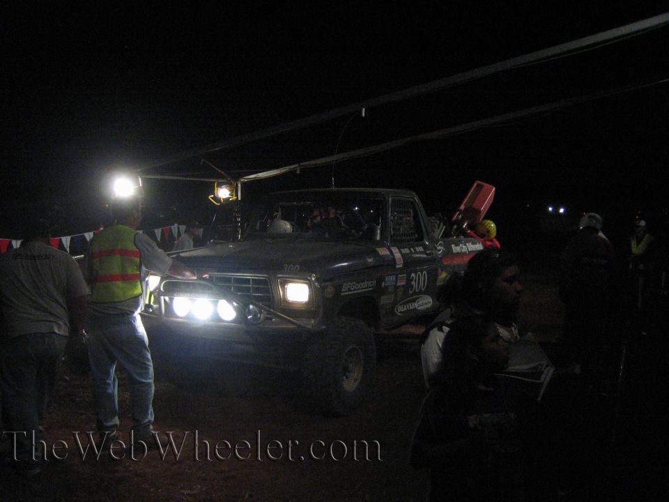 Number 300 off-road truck with lights on among crowd at night