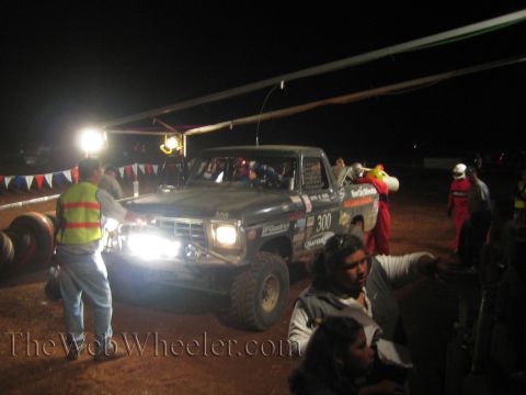 Number 300 off-road truck at lit nighttime pit with crew and bunting