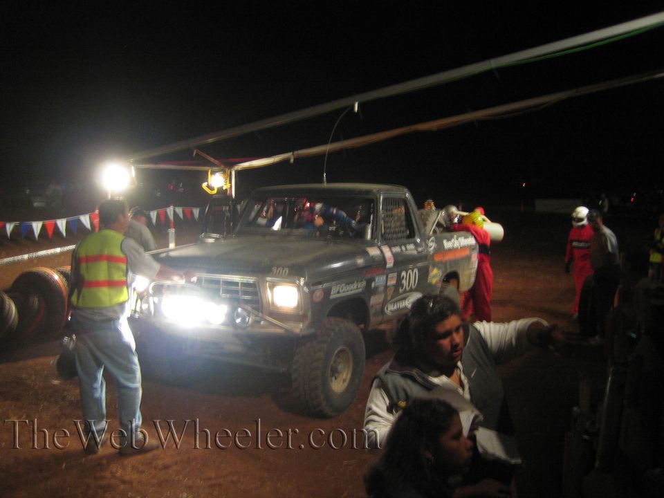 Number 300 off-road truck at lit nighttime pit with crew and bunting
