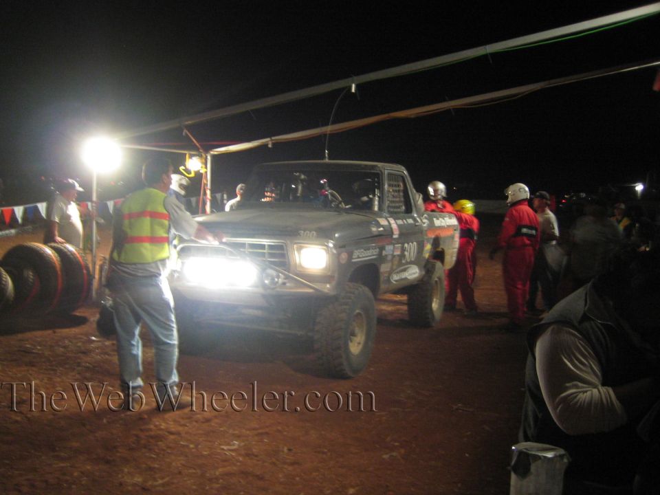 Front view of number 300 off-road truck with crew at night pit