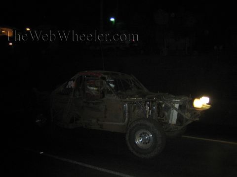 Muddy off-road race truck with headlights on dark road at night
