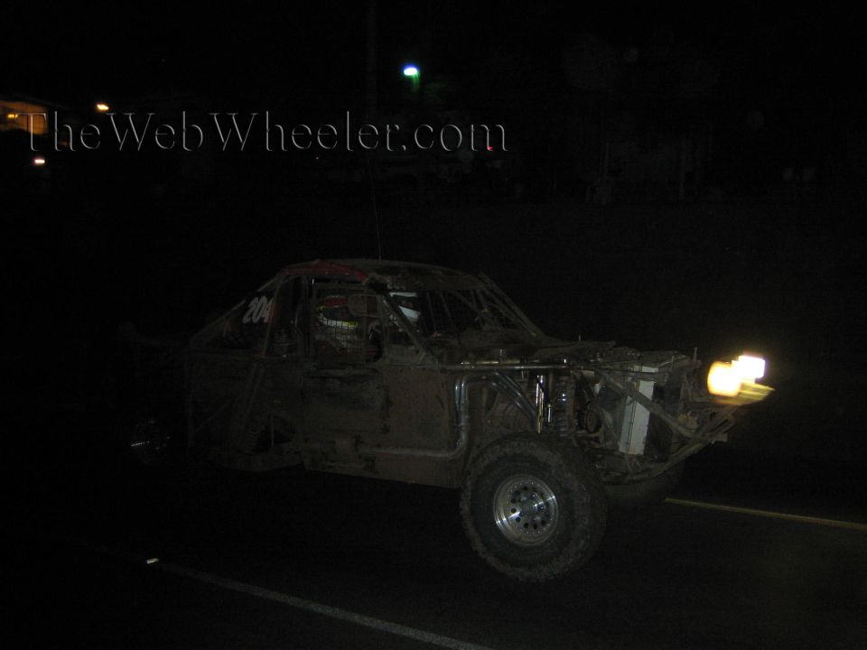 Muddy off-road race truck with headlights on dark road at night