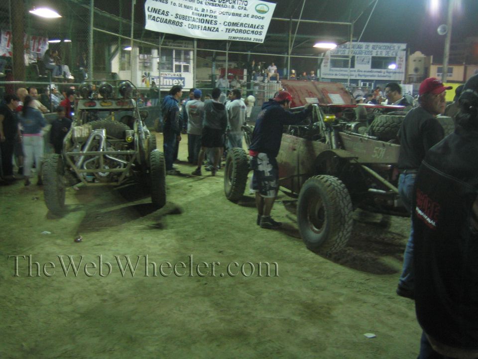 Two tube-frame off-road buggies and a crowd inside a covered arena at night