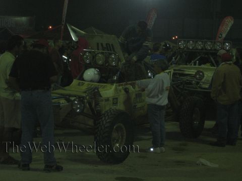Yellow off-road buggies with roof light pods and a crowd at a dim night pit
