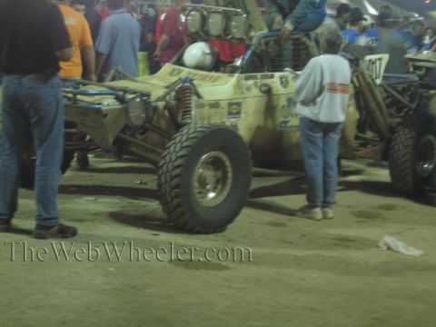 Dusty tan off-road buggy with large tire and roof lights among a crowd at night