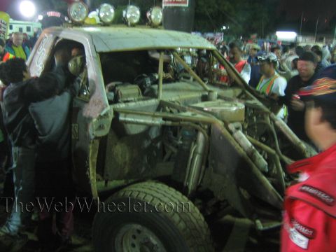 Battered tube-frame off-road race truck with roof lights and exposed engine at night