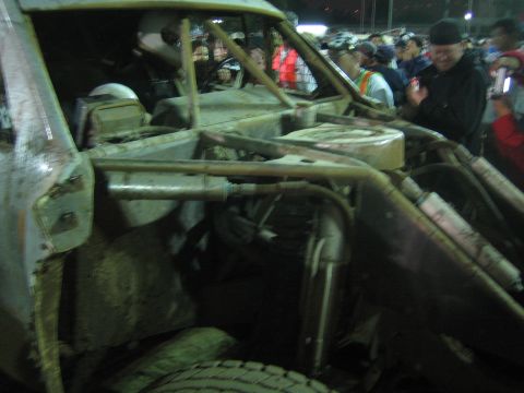 Side view into the exposed tube-frame cockpit and engine of a muddy off-road buggy