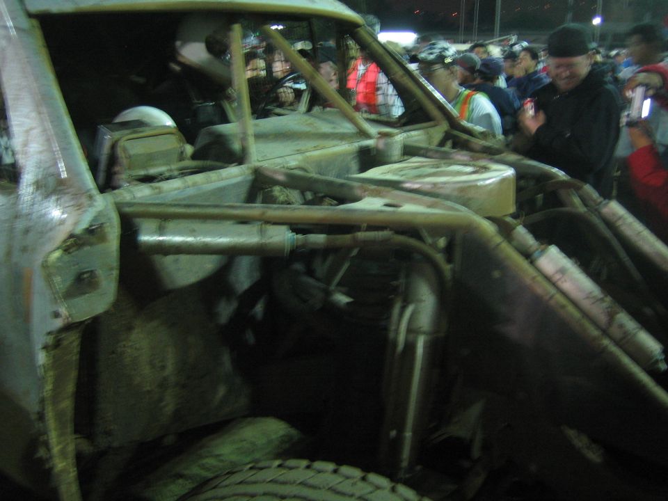 Side view into the exposed tube-frame cockpit and engine of a muddy off-road buggy