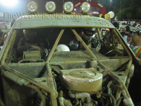 Driver in helmet inside mud-caked off-road truck number 803 with roof light bar