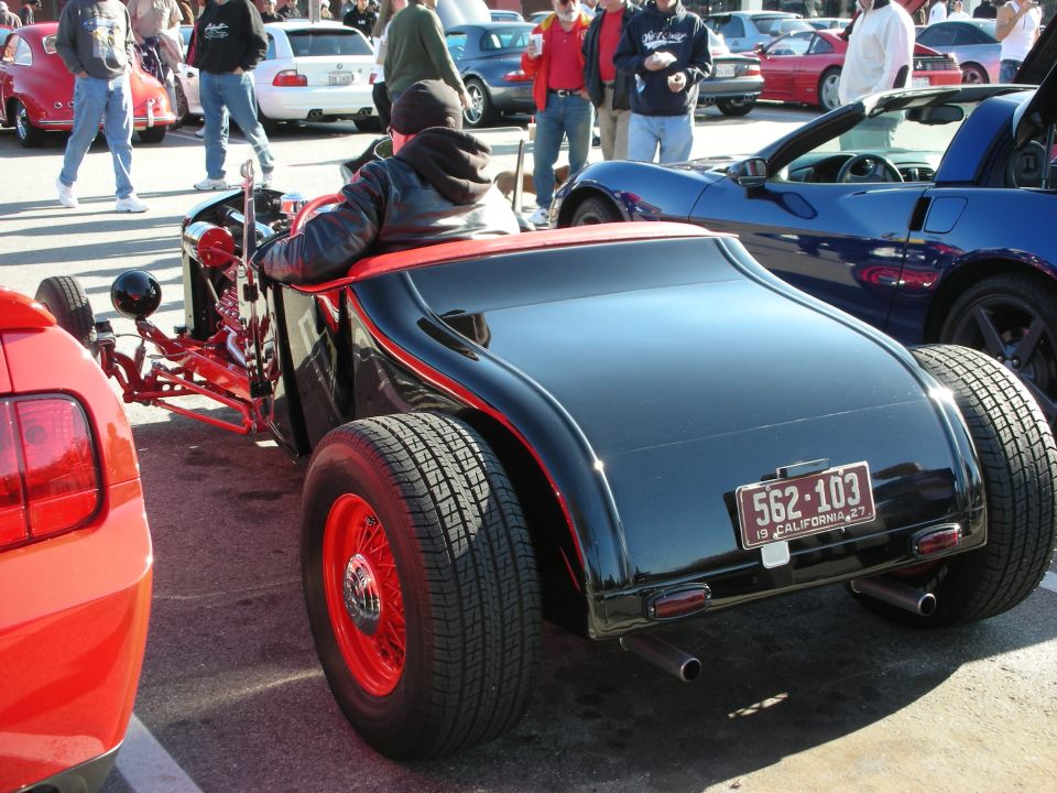 Black hot rod roadster with red wire wheels and California plate at a car meet