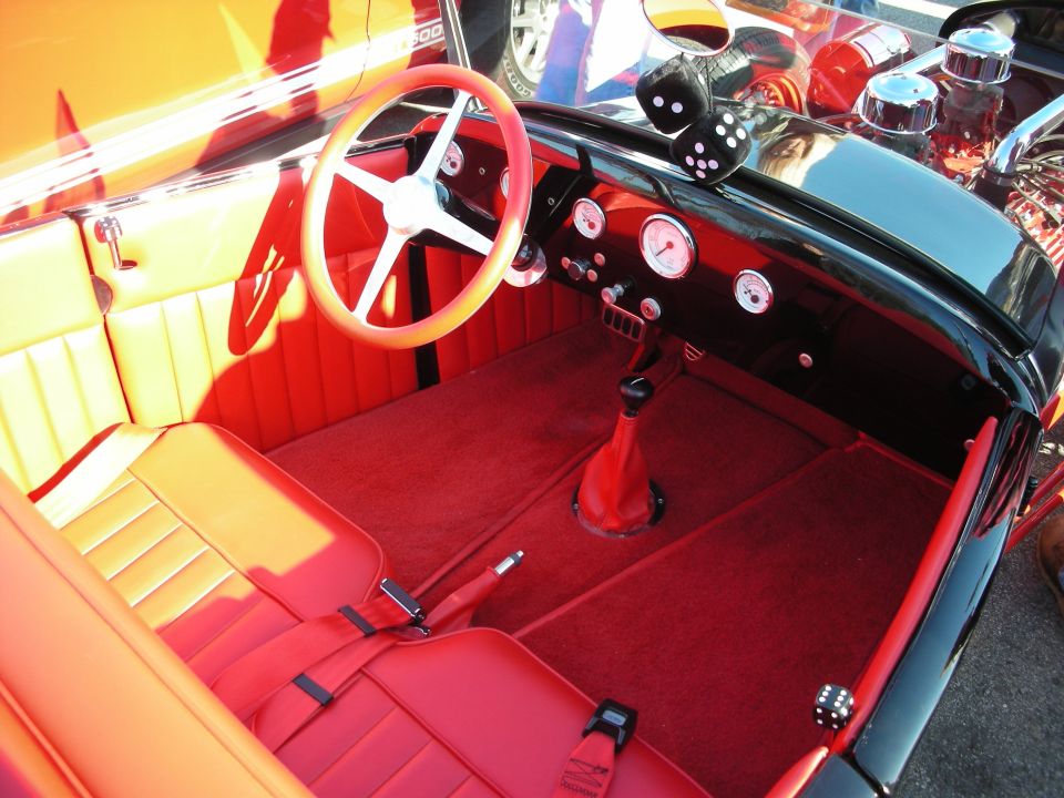 Red and black hot rod interior with white steering wheel, gauges and dice shifter