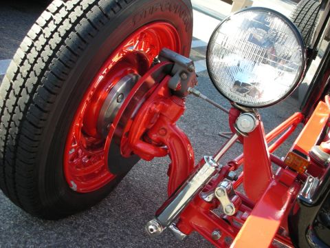 1998 Ford Crown Victoria - Close-up of a hot rod's red wire wheel with Firestone tire, exposed front suspension and a round chrome headlight.
