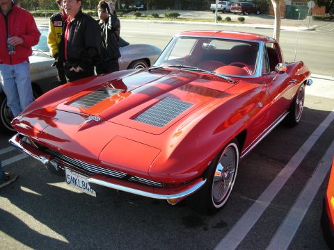 1998 Ford Crown Victoria - red mid-1960s Corvette Sting Ray coupe with hood louvers and chrome bumpers parked at an outdoor car meet.