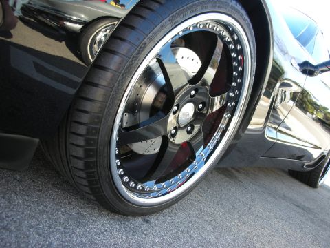 1998 Ford Crown Victoria - Detail of a black sports car's chrome-lipped multi-spoke wheel over a drilled brake rotor and red caliper.