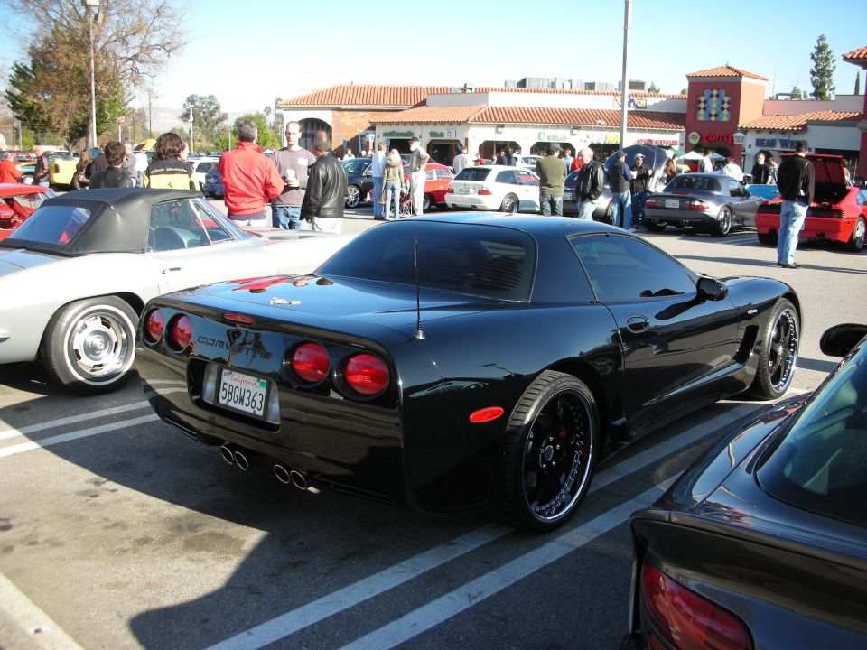 Black C5 Chevrolet Corvette coupe rear three-quarter at a busy car meet