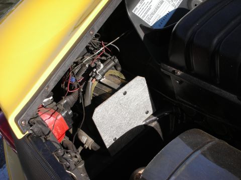 1998 Ford Crown Victoria - Engine-bay corner of a yellow vehicle showing wiring harnesses, red and black components and a riveted metal box.