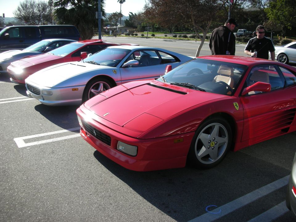 Red Ferrari coupe beside a silver Ferrari in a parking lot at a car meet