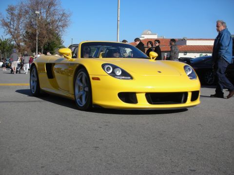 1998 Ford Crown Victoria - yellow Porsche Carrera GT supercar parked as a man in a blue jacket walks past at an outdoor car meet.