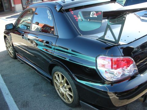 1998 Ford Crown Victoria - black Subaru Impreza sedan parked in a lot, fitted with a large adjustable rear wing and gold multi-spoke wheels.