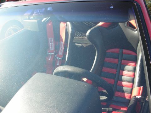 1998 Ford Crown Victoria - View through a windshield of a car interior with black-and-red sport seats and red four-point racing harnesses.